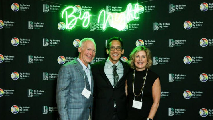 Three people posing in front of a branded backdrop with 'Big Brothers Big Sisters' logos.